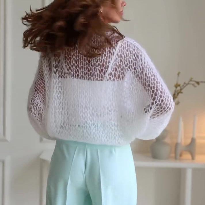 Person wearing a sheer top and light blue pants in a neutral setting