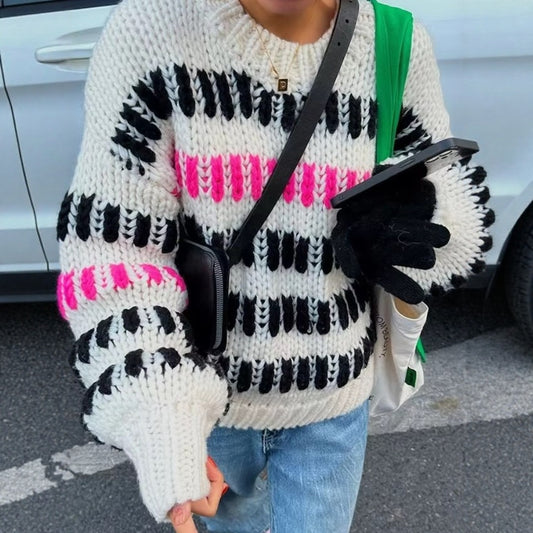 Person wearing a patterned sweater with black, pink, and white stripes, holding a phone.