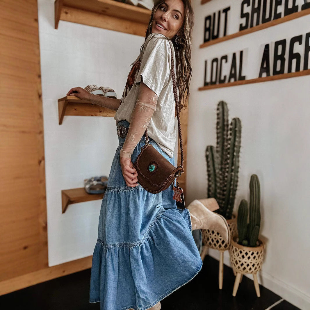 Woman in a denim dress holding a brown leather bag in a room with wooden shelves and cacti.