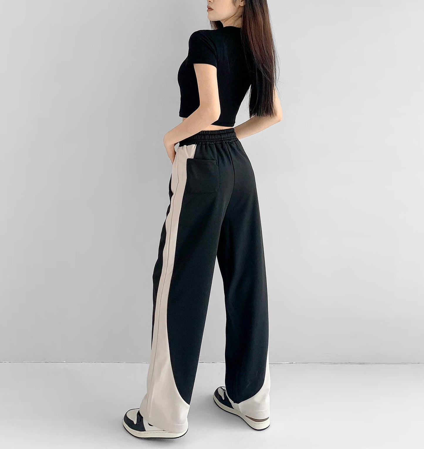 Woman wearing a black top and black and white pants against a gray background