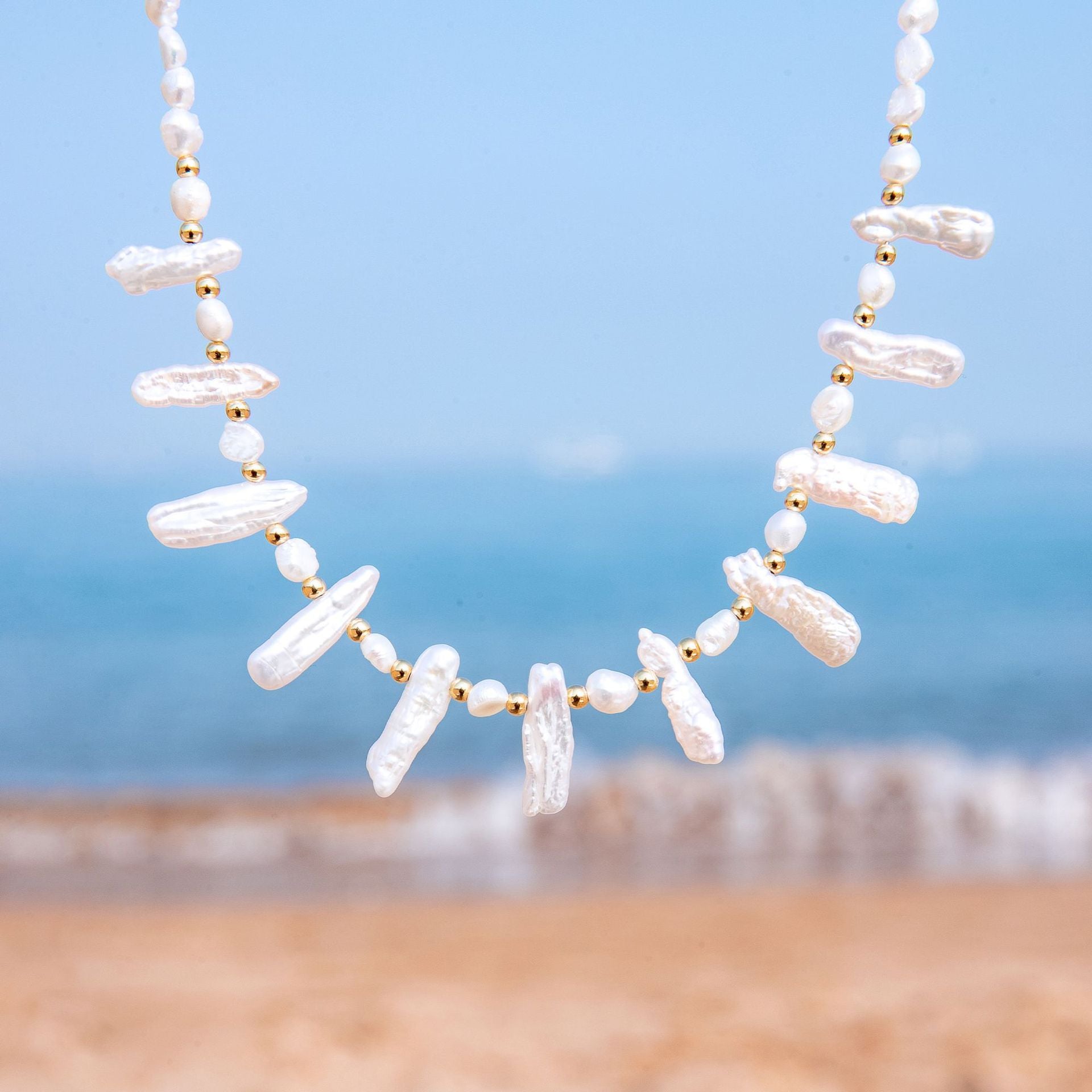 Pearl necklace with gold accents against a beach background