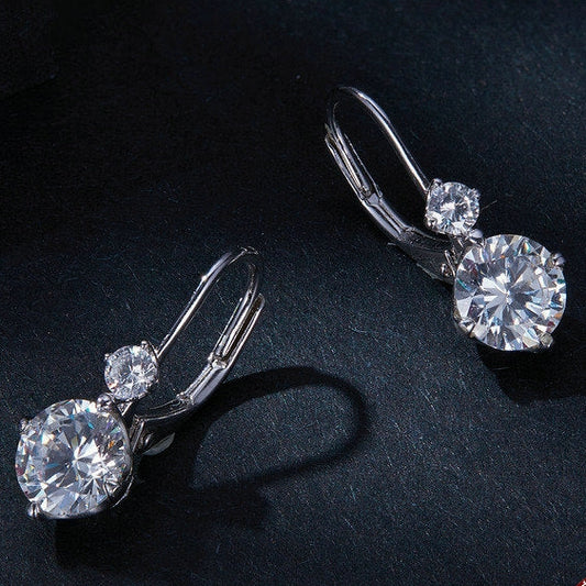 Pair of silver earrings with clear gemstones on a dark background, featuring a 'Real Sterling Silver 925' stamp.