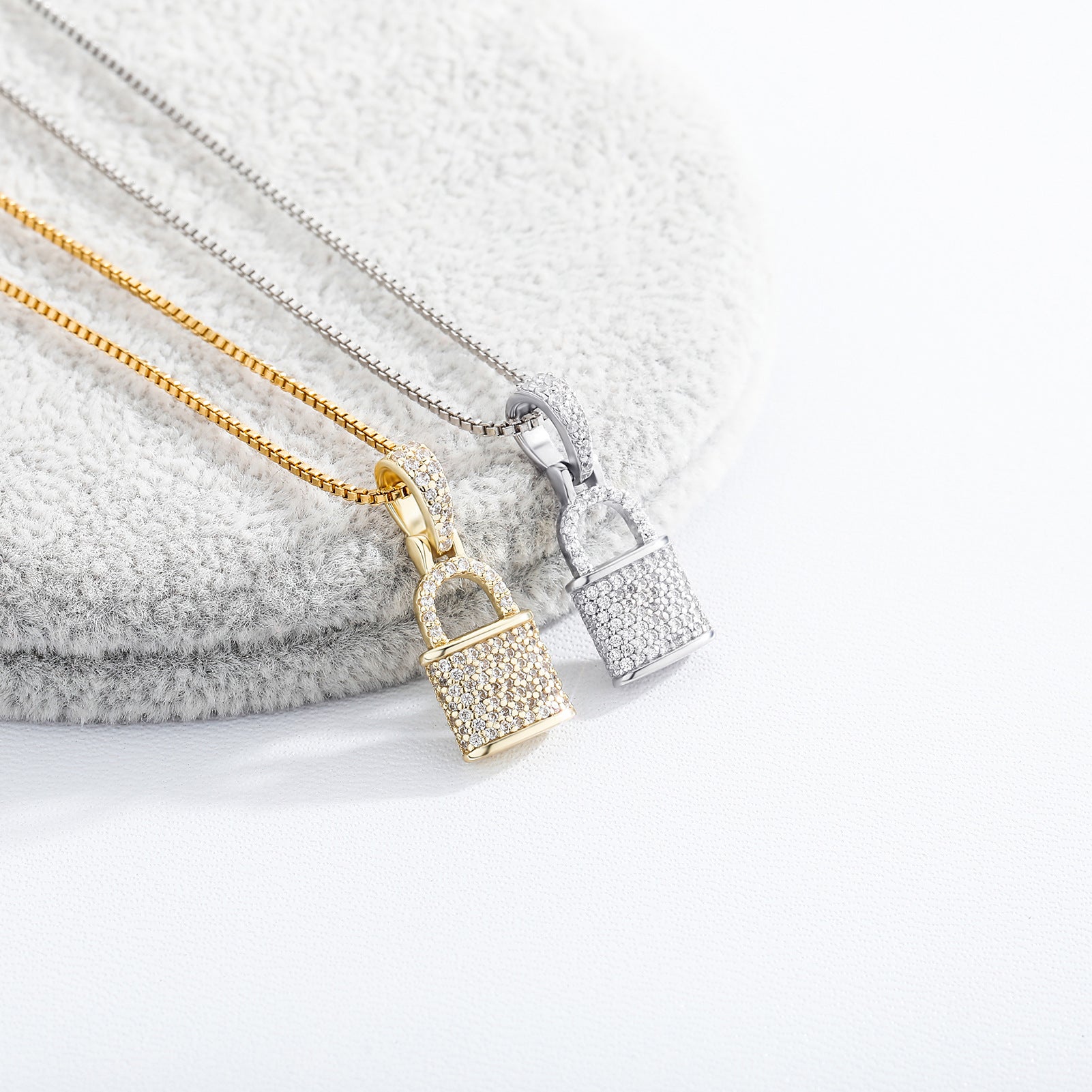 Two gold padlock-shaped pendants on chains against a textured surface.