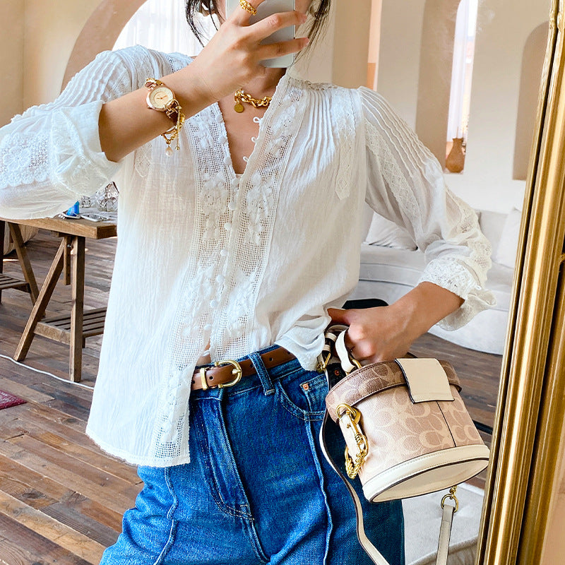 Person wearing a white lace top and blue jeans, holding a beige handbag.