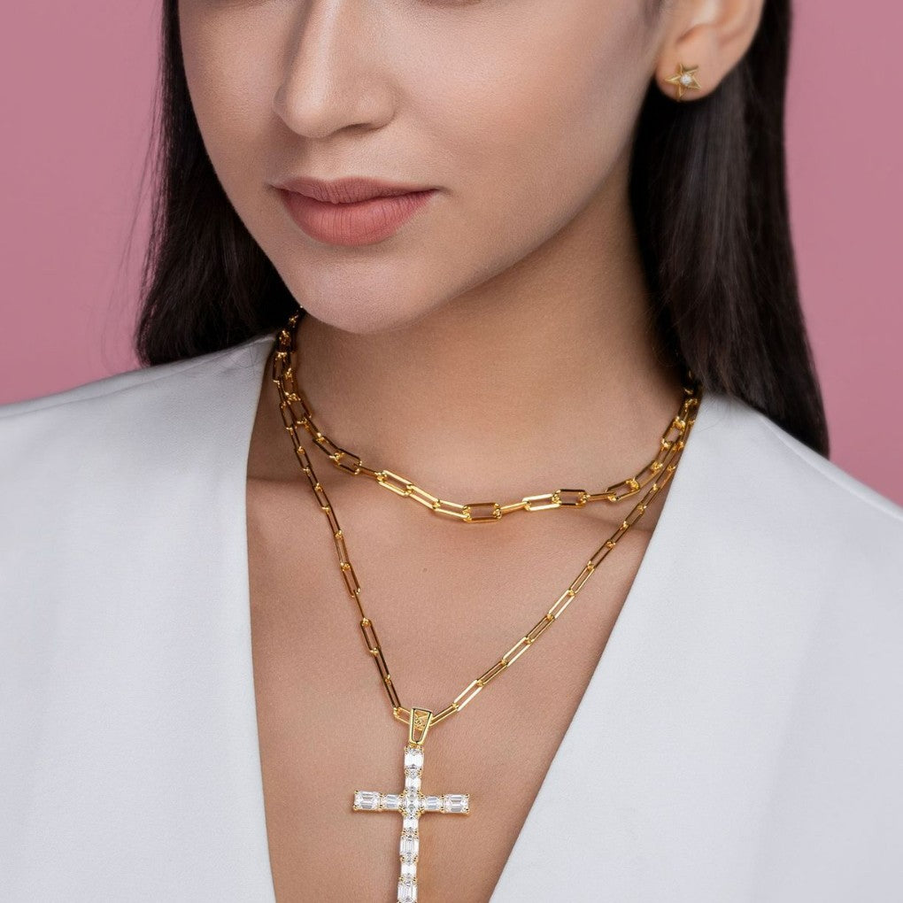 Woman wearing a gold chain necklace with a cross pendant against a pink background