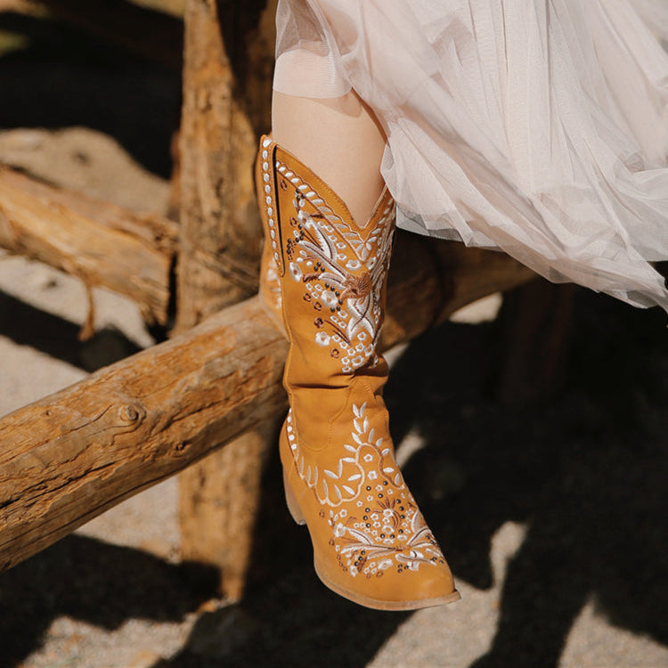 Person wearing tan cowboy boots with white embroidery sitting on a wooden fence.