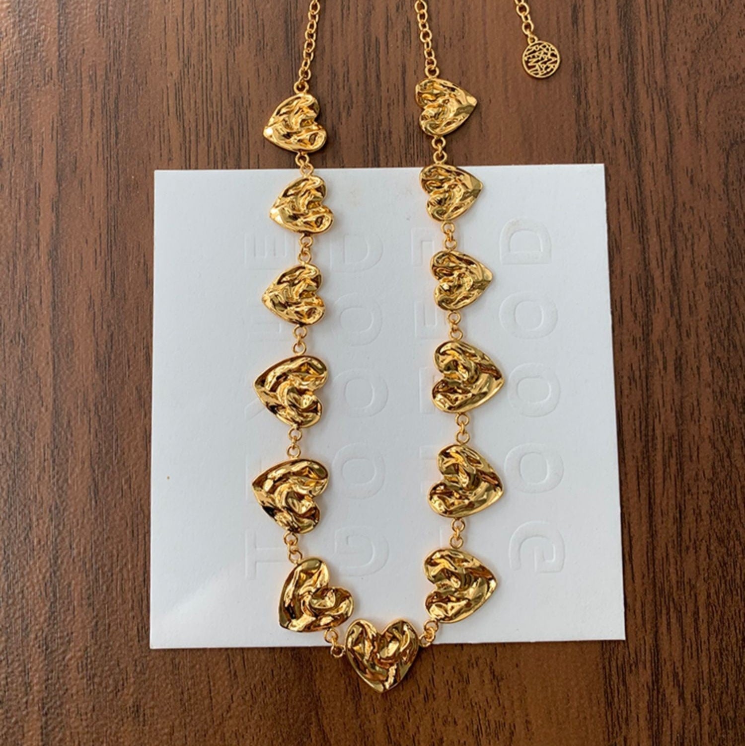 Gold necklace with heart-shaped pendants on a white card against a wooden background