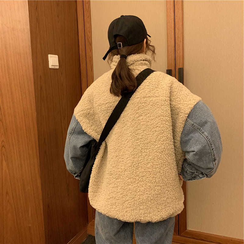 Person wearing a beige fleece vest over a denim jacket in a room with wooden doors.