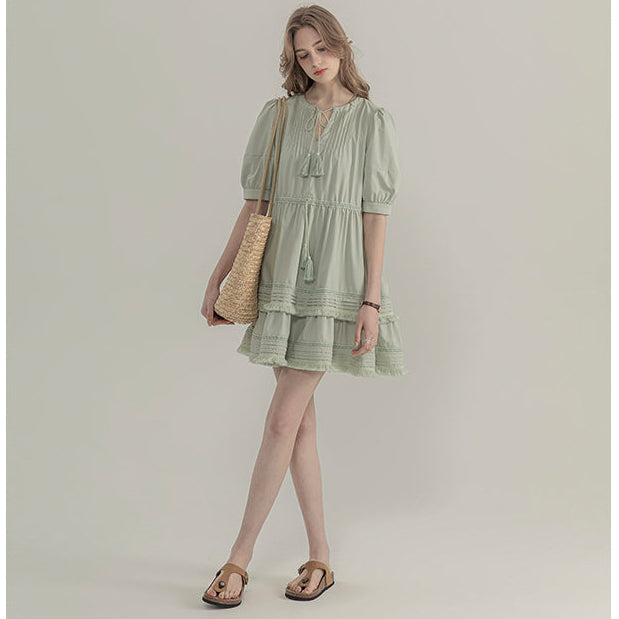 Woman wearing a light green dress holding a woven bag on a plain background