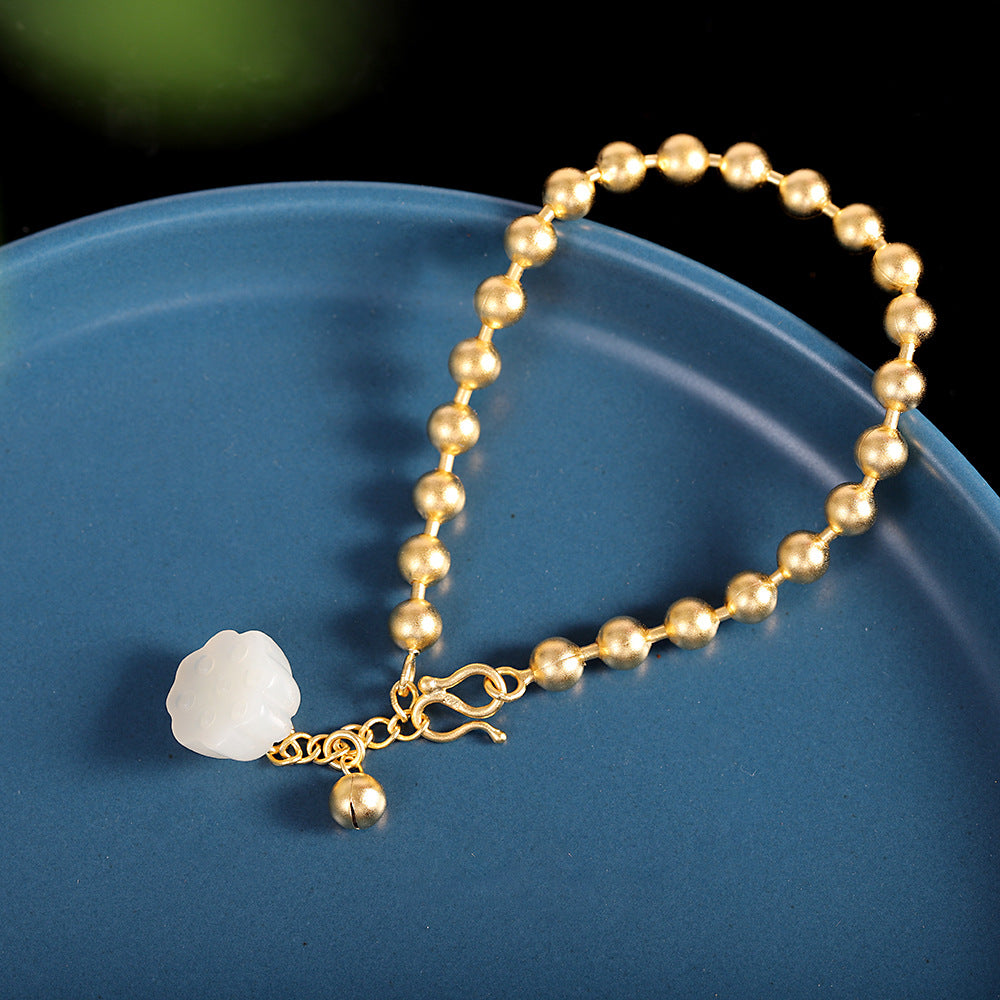 Gold beaded bracelet with a white stone charm on a blue surface