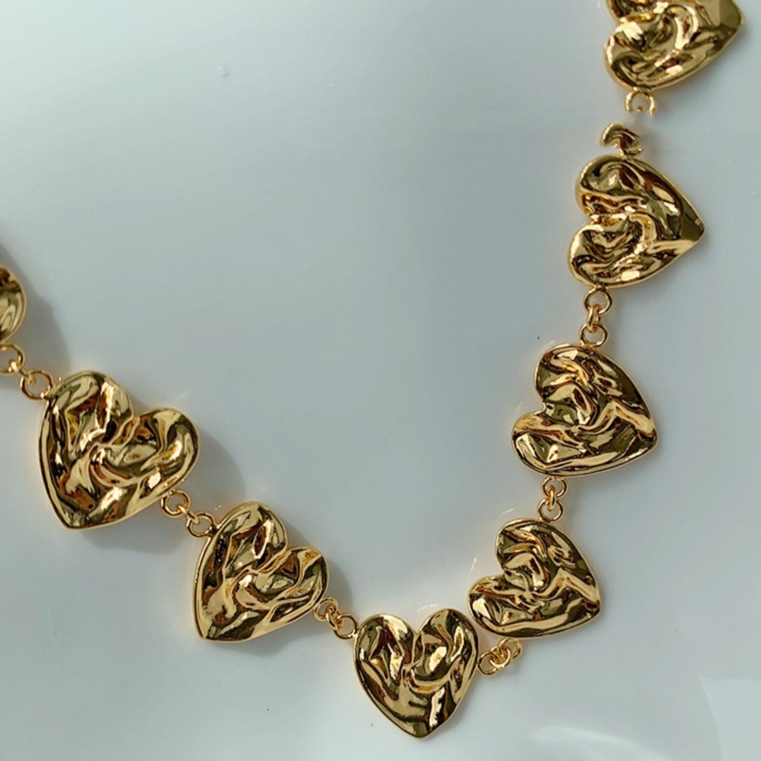 Gold necklace with heart-shaped links on a white background