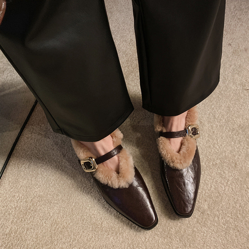 Brown pointed-toe shoes with fur trim worn by a person in black pants on a carpeted floor.