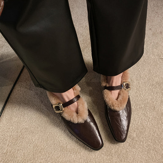 Brown pointed-toe shoes with fur trim worn by a person in black pants on a carpeted floor.
