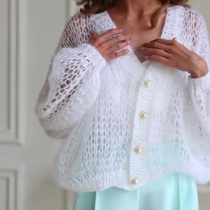 Woman wearing a white lace cardigan with pearl buttons against a neutral background