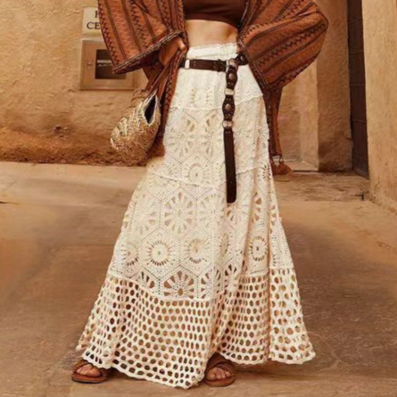 Person wearing a long white lace skirt with a brown top and sandals, standing in a sandy area.