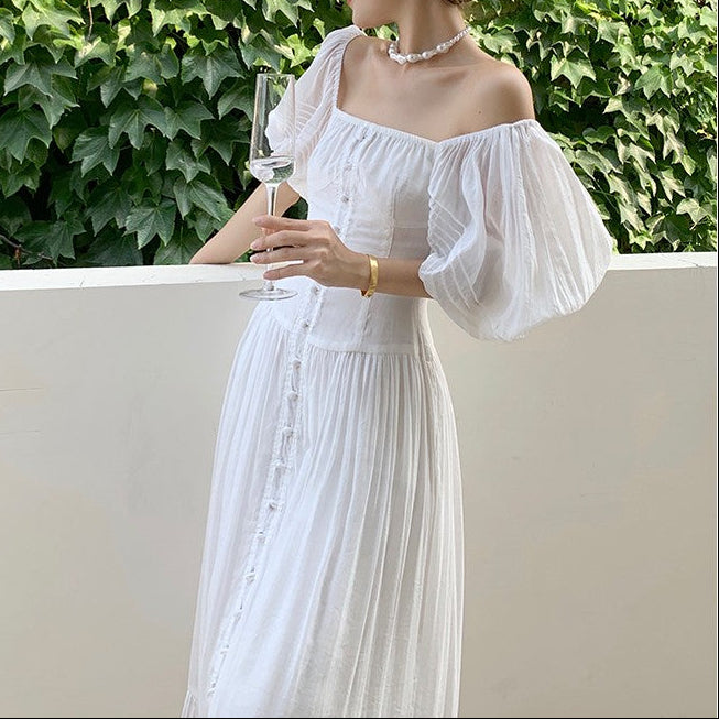 Woman in a white dress holding a glass against a green ivy background