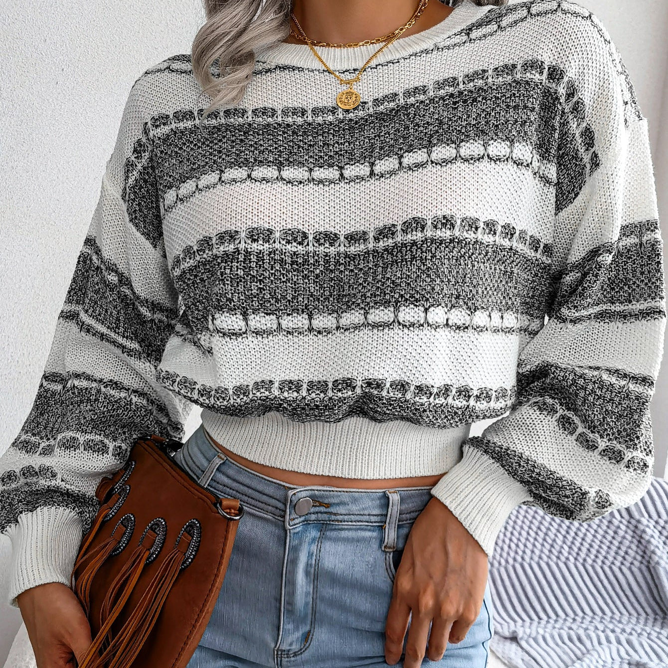 Person wearing a striped sweater and jeans, holding a brown leather bag.