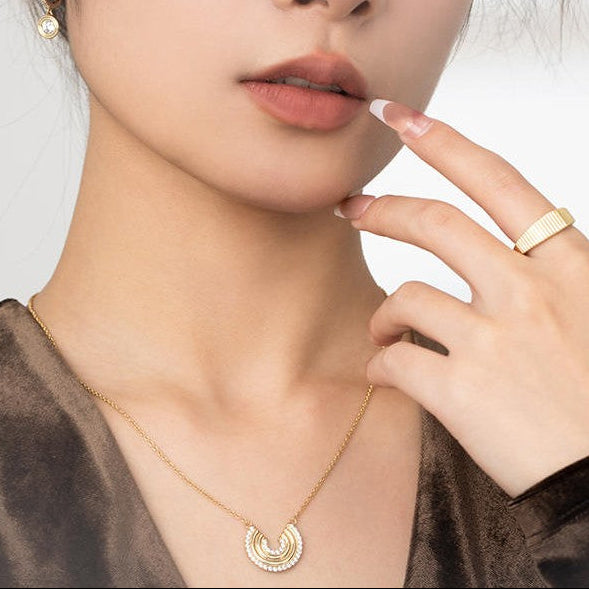 Woman wearing gold jewelry including a necklace, earrings, and ring on a neutral background