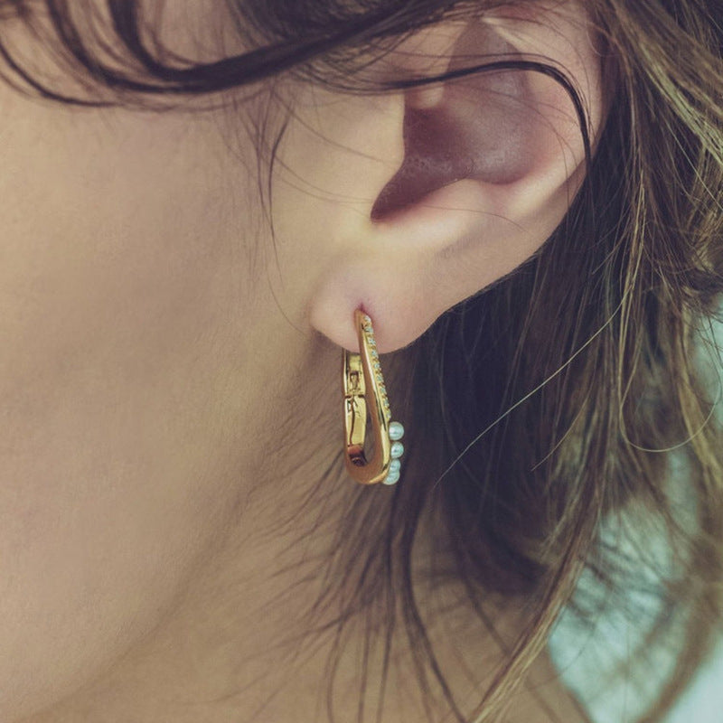 Close-up of an ear wearing a gold hoop earring with small stones.