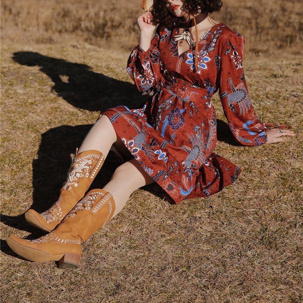 Woman in a patterned dress and cowboy hat sitting in a field