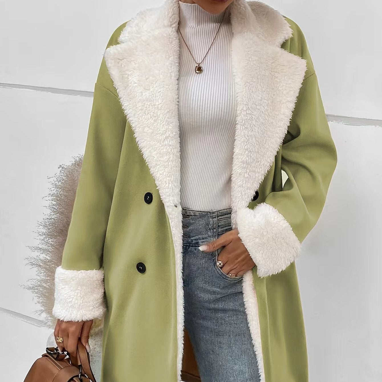 Person wearing a green coat with white fur lining, holding a brown bag against a light background