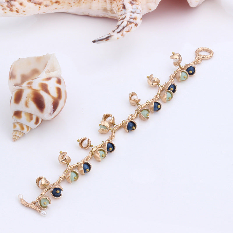 Gold bracelet with blue and green accents on a white background with shells.