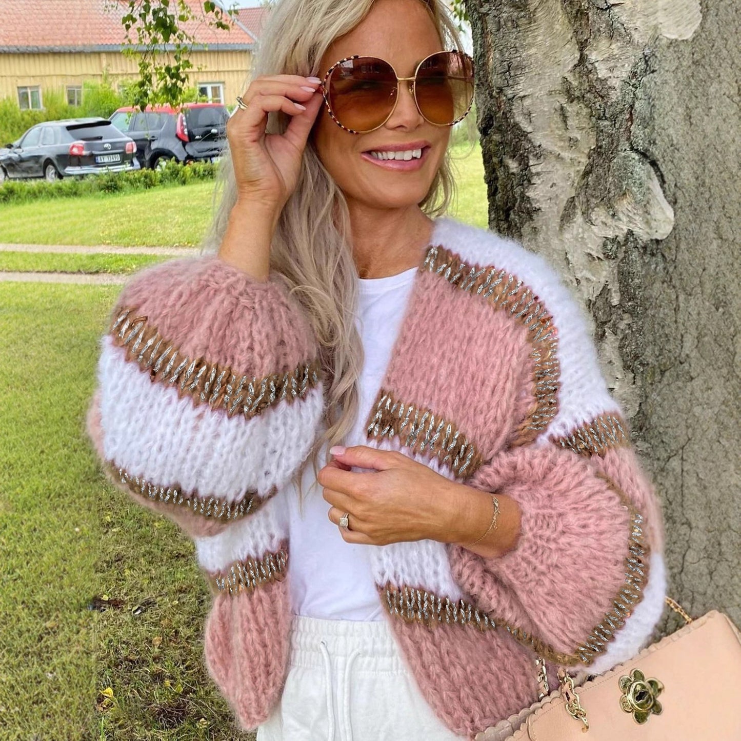 Woman wearing a pink and white cardigan with gold accents, standing outdoors.