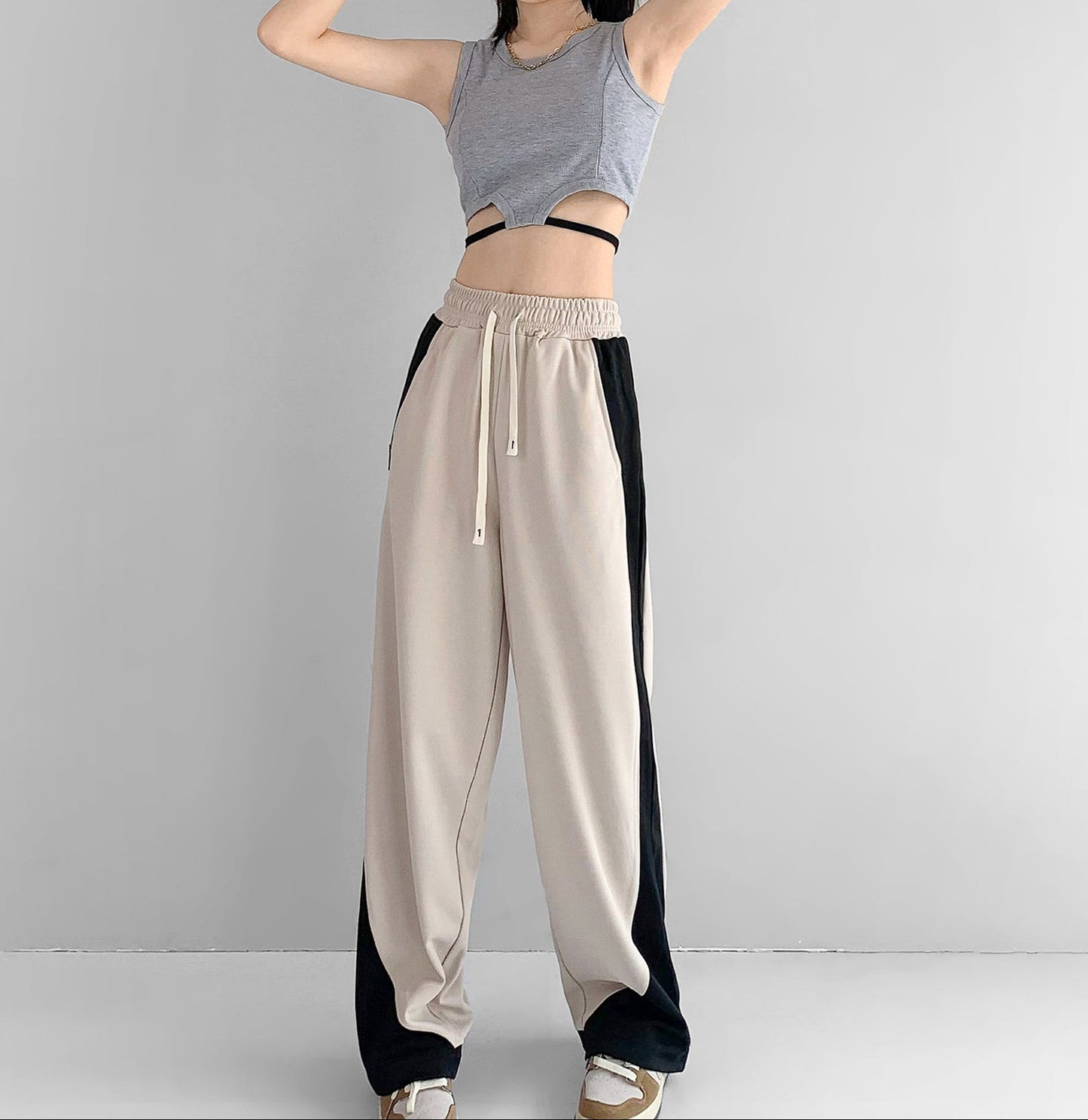 Person wearing a gray tank top and beige pants with black sides on a plain background