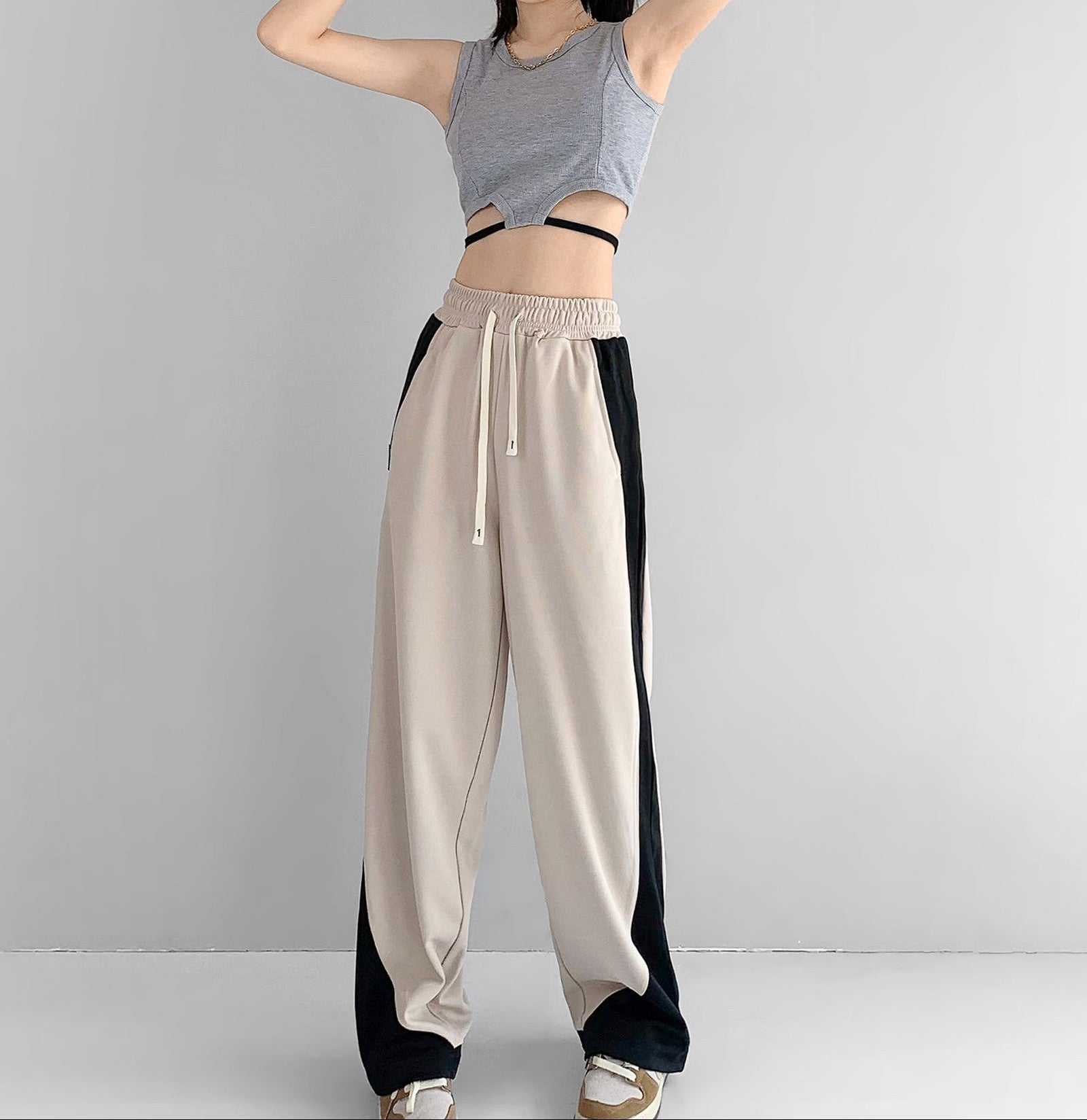 Person wearing a gray tank top and beige pants with black sides on a plain background