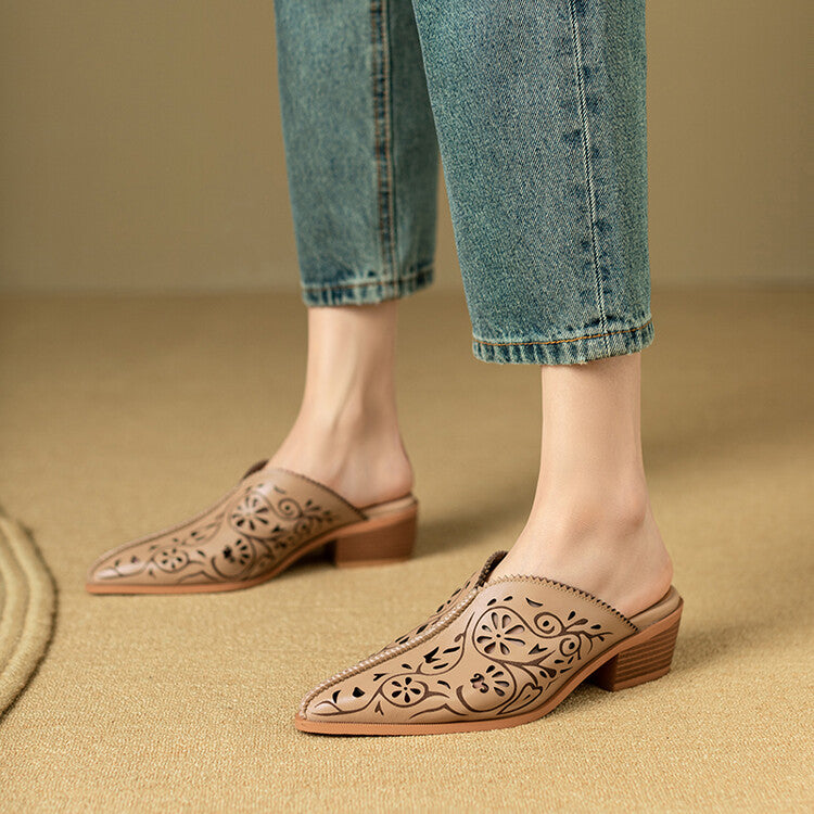 Brown leather mules with floral patterns worn with blue jeans on a beige carpet.