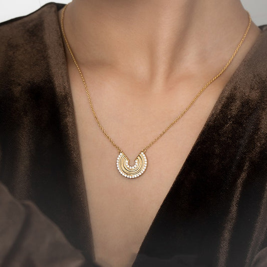 Gold necklace with a circular pendant on a person wearing a brown garment.