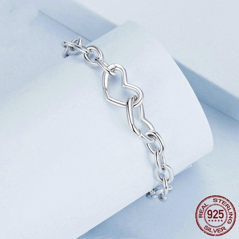 Silver bracelet with a heart design on a light blue geometric background, featuring 'Real Sterling Silver 925' stamp.