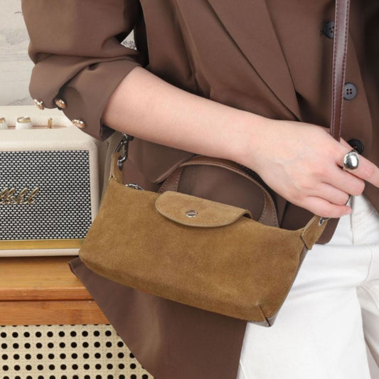 Person holding a brown suede handbag with a blurred background