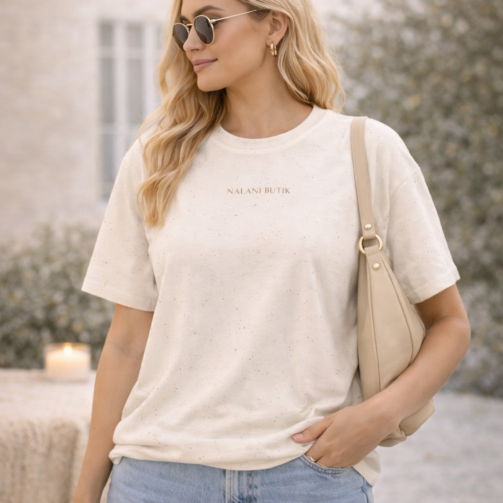 Woman wearing a beige t-shirt with 'Nalan Ebru' text, holding a beige bag outdoors.
