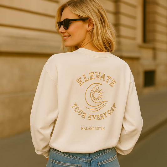 Woman wearing a beige sweatshirt with text and logo, standing against a beige wall.