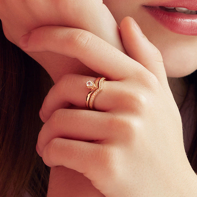 Close-up of a hand wearing a gold ring with a diamond, touching the ear.