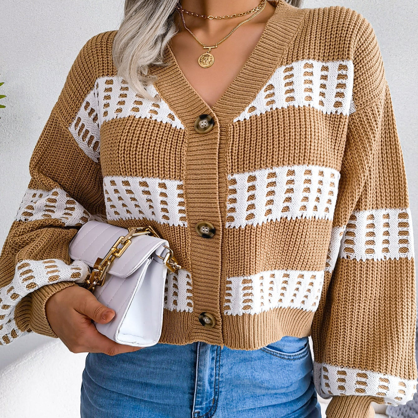 Person wearing a brown and white patterned cardigan with blue jeans against a plain background