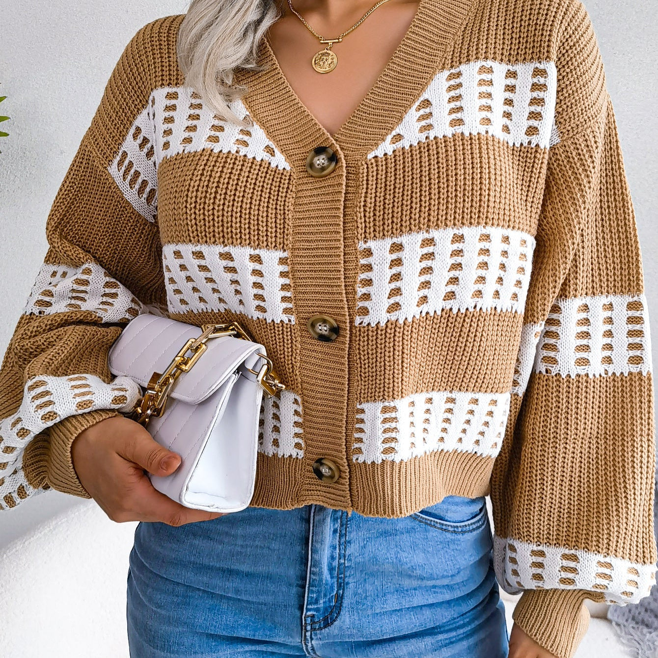 Person wearing a brown and white patterned cardigan with blue jeans against a plain background