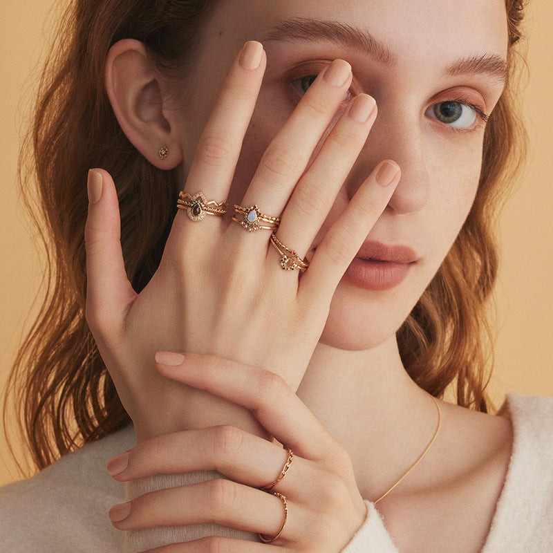 Close-up of a woman's hand wearing multiple gold rings on a beige background