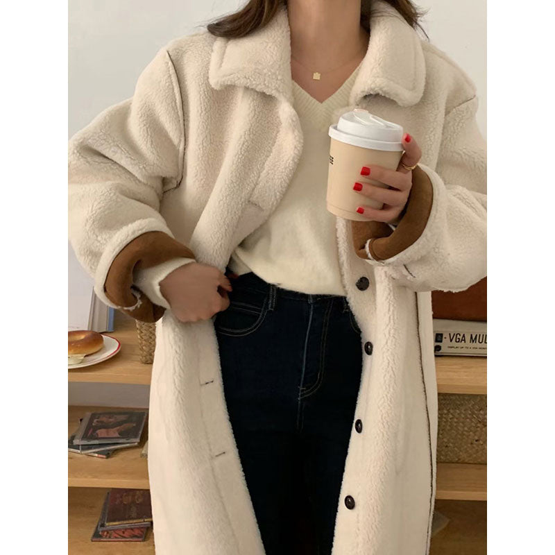 Person wearing a beige sherpa coat holding a coffee cup indoors.