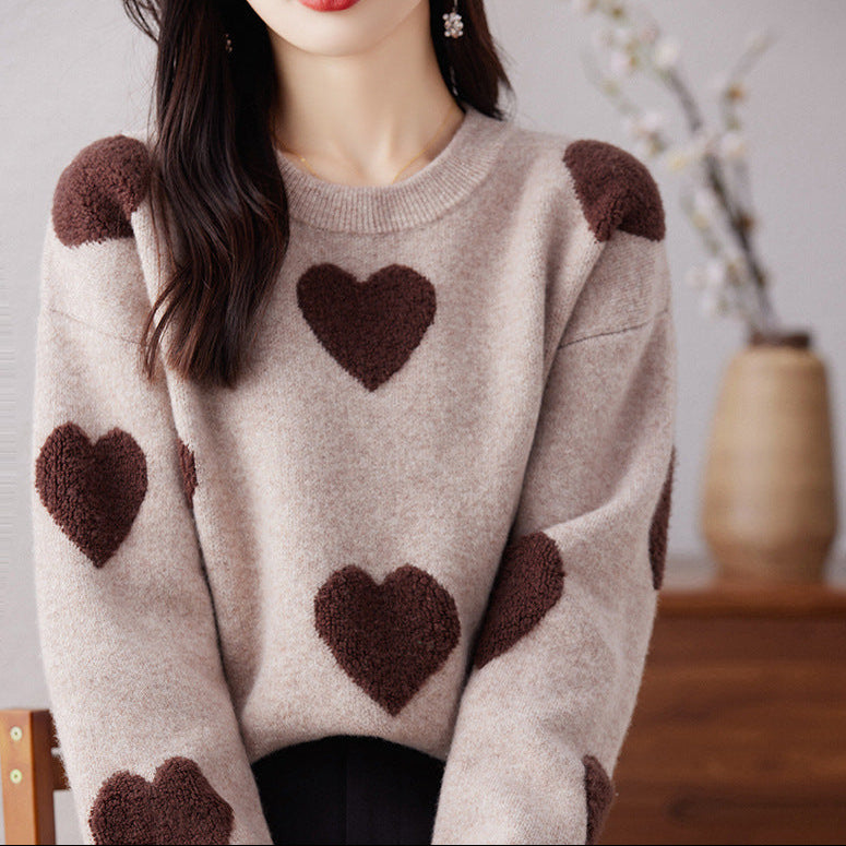Person wearing a beige sweater with brown heart patterns in a blurred indoor setting