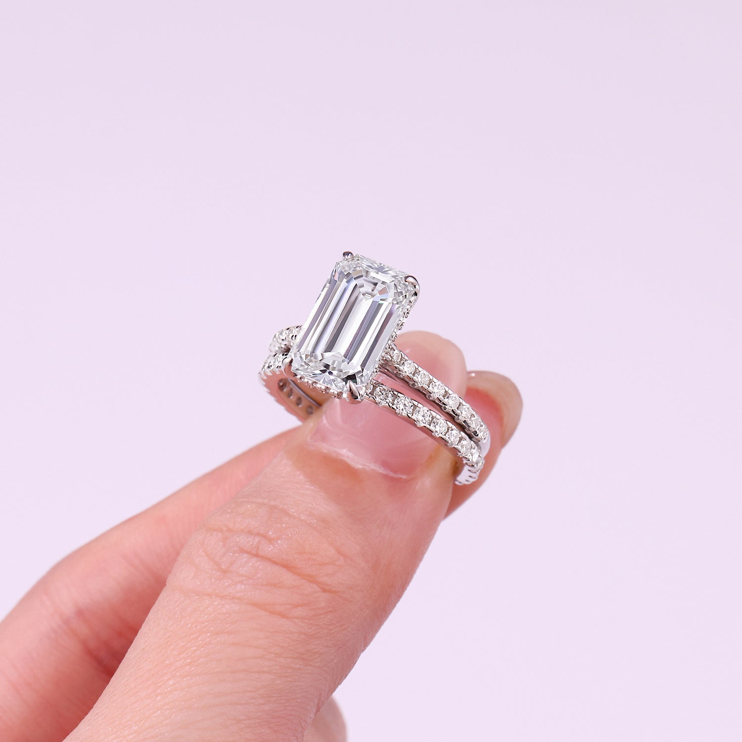 Diamond ring held by a hand against a light purple background
