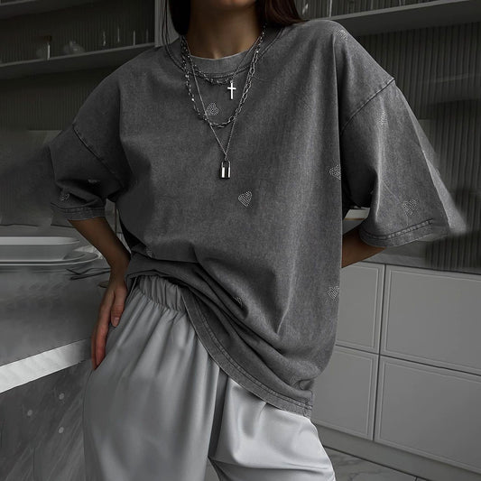 Person wearing an oversized gray t-shirt and light gray pants in a minimalistic room.