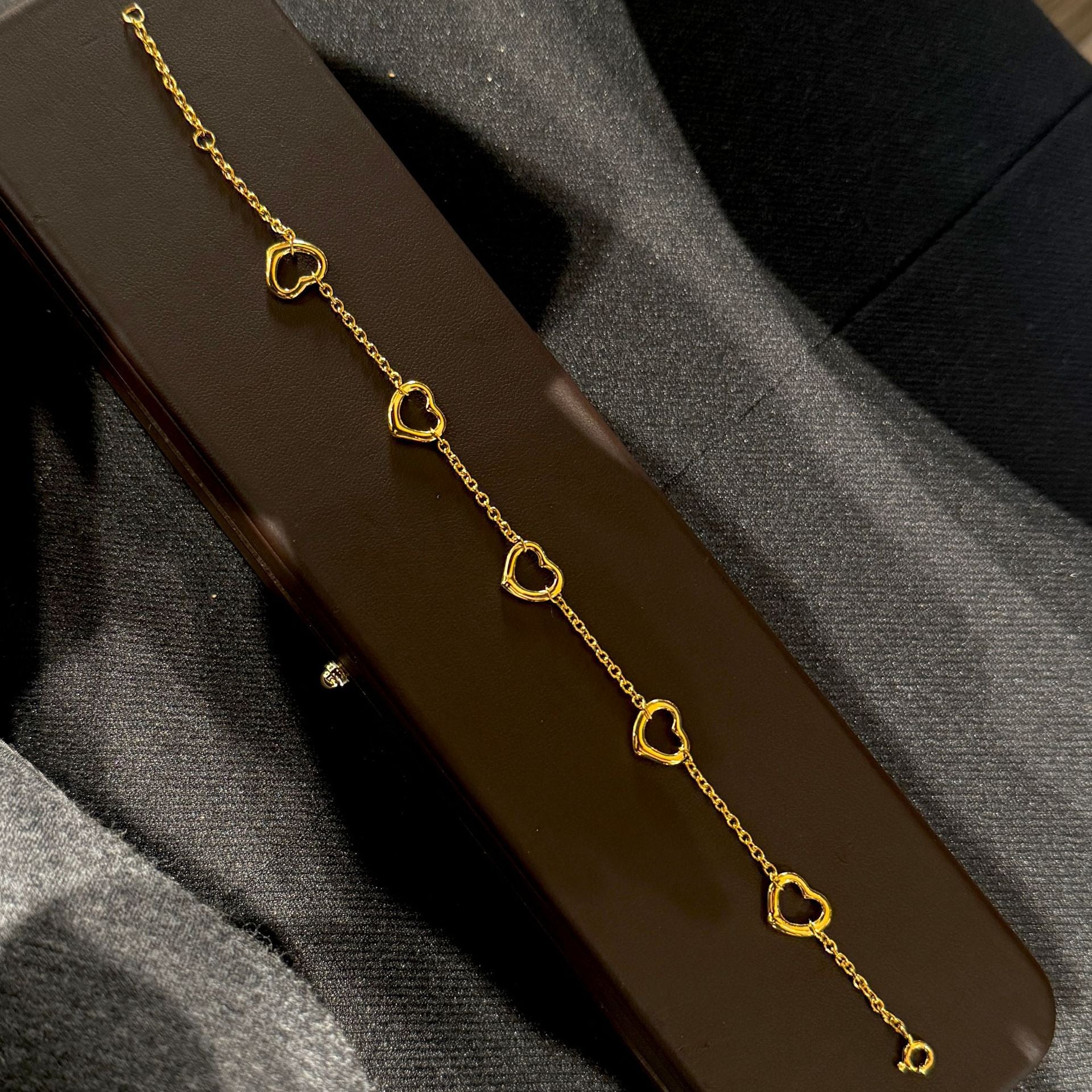 Gold heart-shaped bracelet on a dark brown surface with gray fabric background