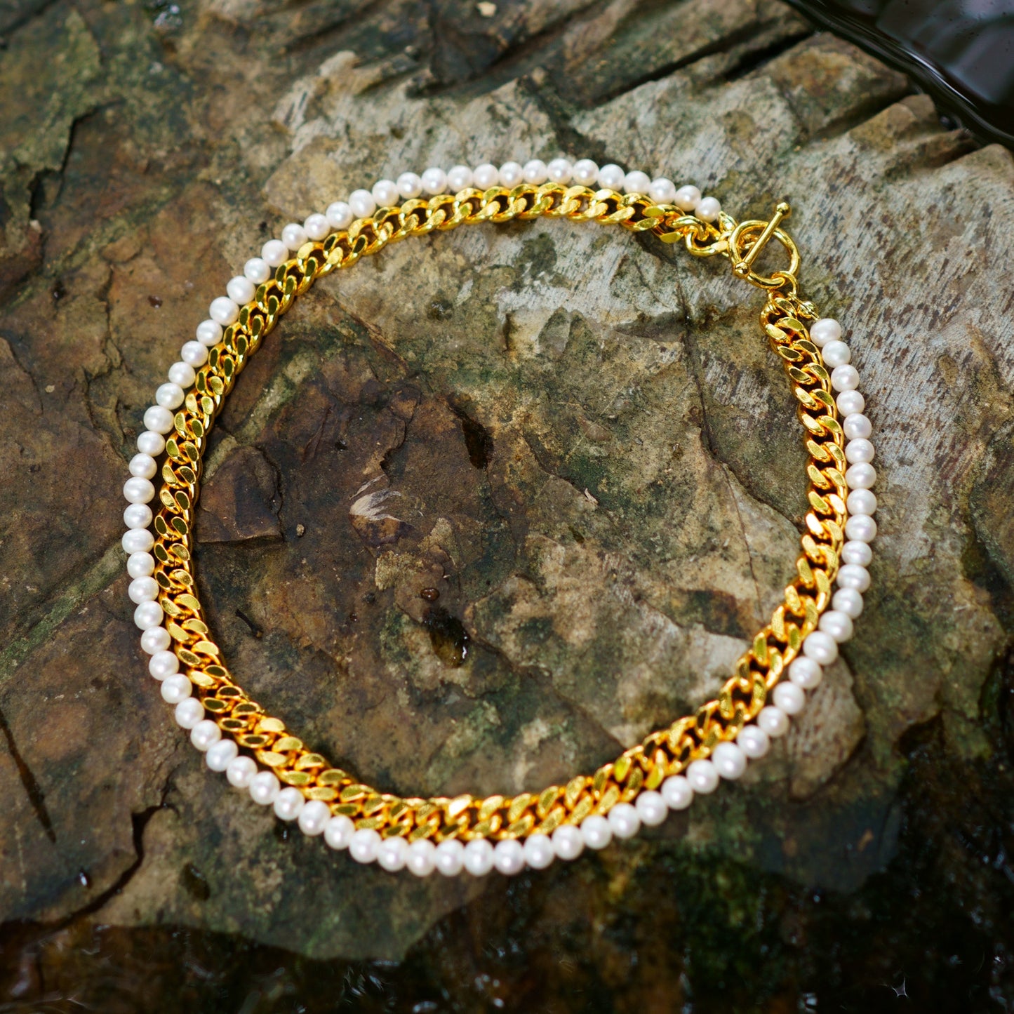 Gold chain and pearl bracelet on a textured stone surface