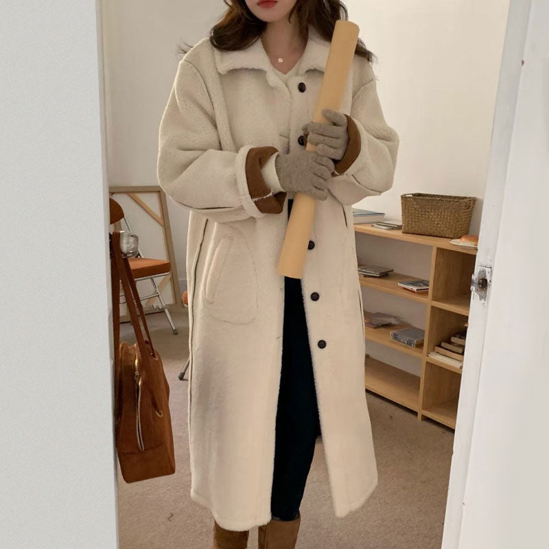 Person wearing a long beige coat holding a wooden object in a room with furniture.