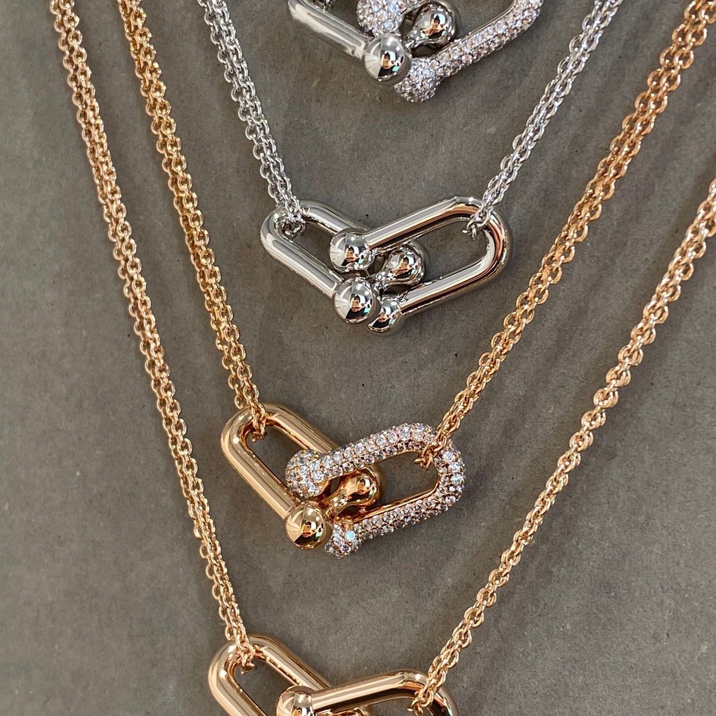 Three necklaces with heart-shaped pendants in gold, silver, and rose gold on a gray background.