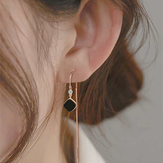 Close-up of an ear wearing a rose gold earring with a black gemstone on a neutral background