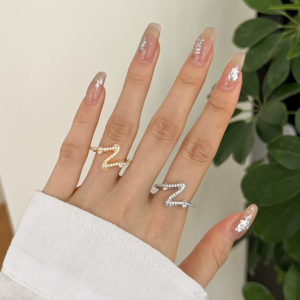 Hand with decorative rings and glittery nails against a neutral background