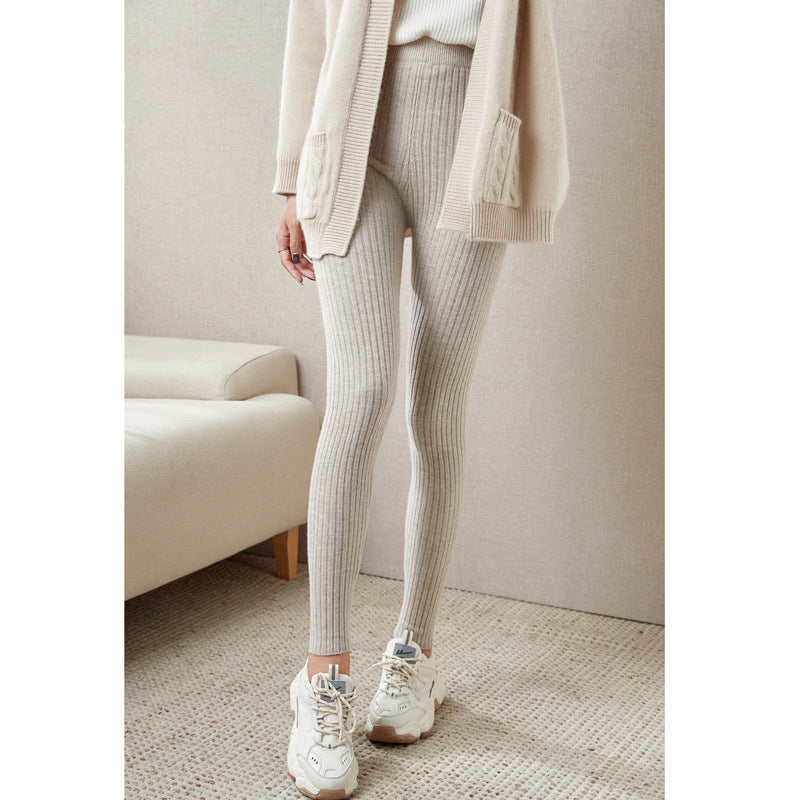 Person wearing light gray ribbed leggings with a beige coat in a neutral room.